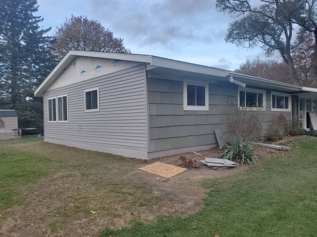 Gray single-story house with white trim and a grassy yard under cloudy skies.
