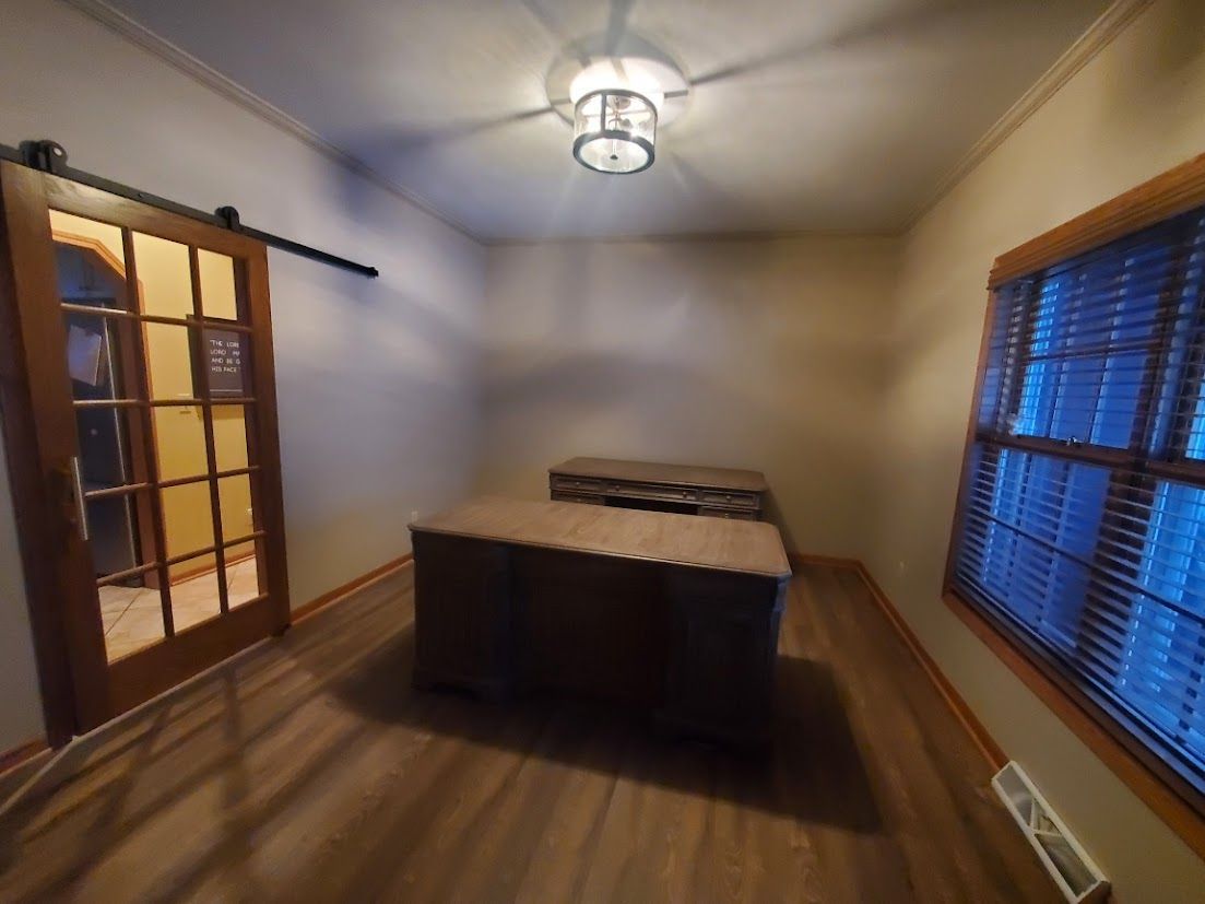 Empty room with wood floors, a central cabinet, glass doors, and a window with blue blinds.