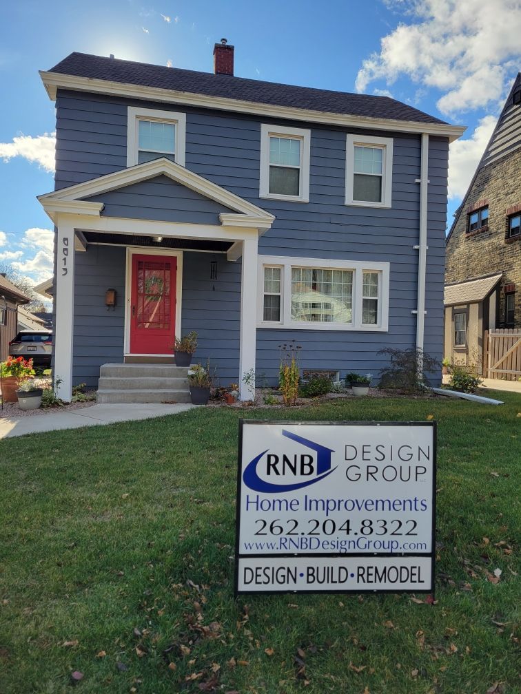 Blue two-story house with red door and a Home Improvements sign on the lawn