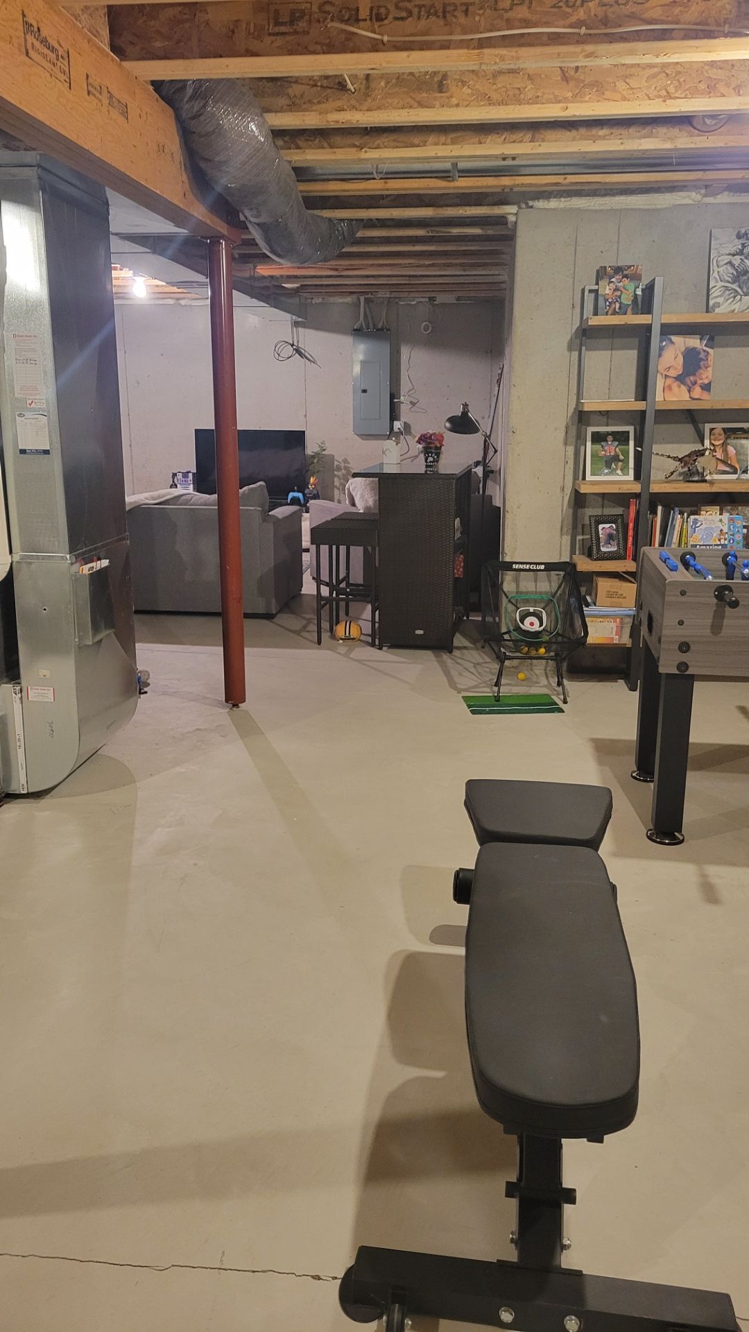 Basement home gym with bench, weight rack, exercise equipment, exposed ceiling beams, and storage shelves