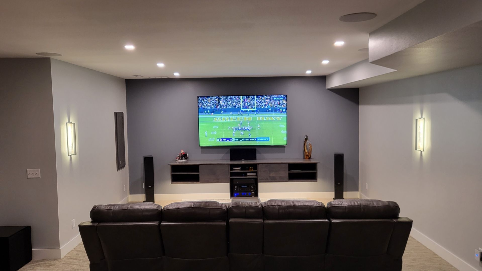 Basement home theater with leather recliner, wall-mounted TV, and recessed lighting