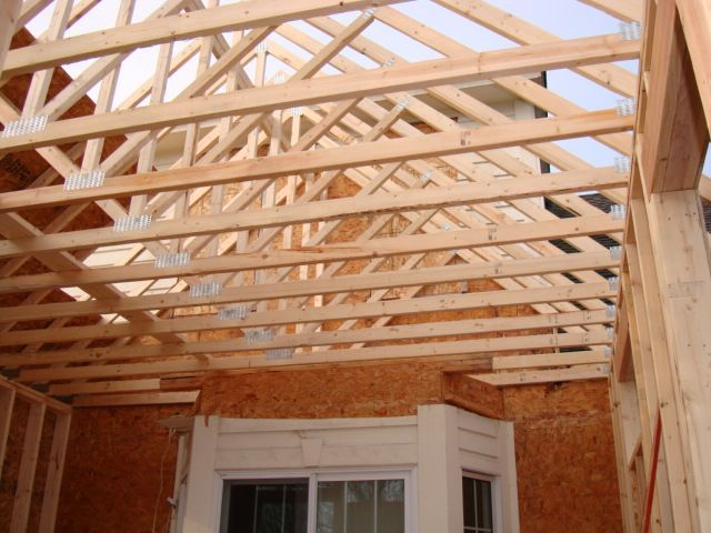 Wooden roof trusses over a partially framed room interior with a window and exposed plywood walls