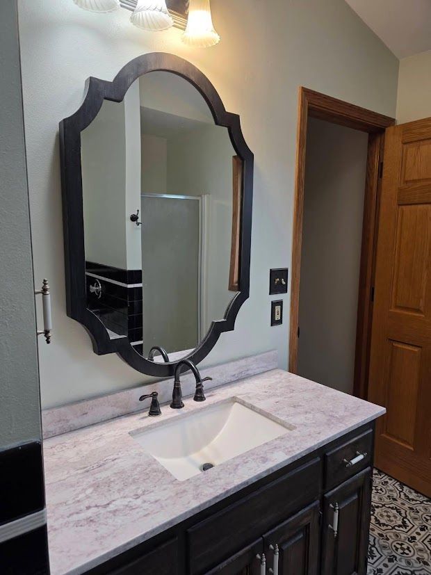 Bathroom vanity with framed mirror, marble countertop, and wall sconce in a narrow room