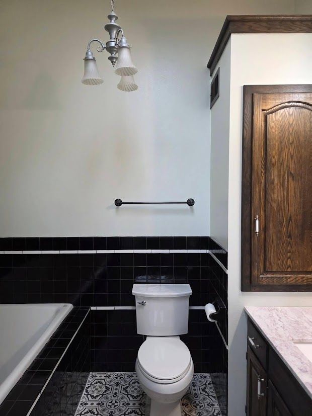 Bathroom with white toilet, black tile wainscoting, and wood vanity beside a bathtub.