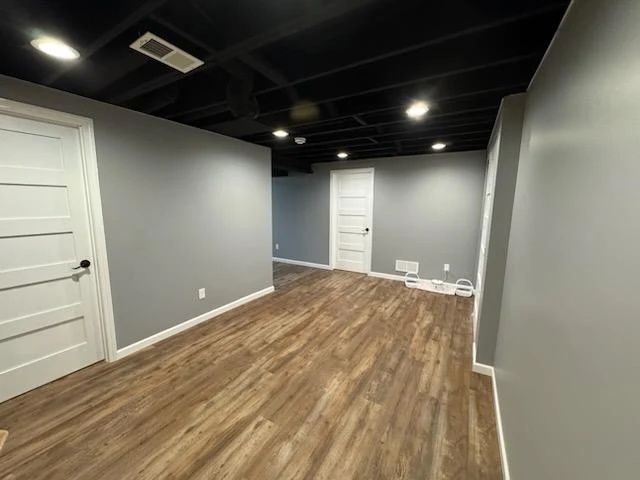 Empty room with wood-look flooring, brown walls, and an open white door.