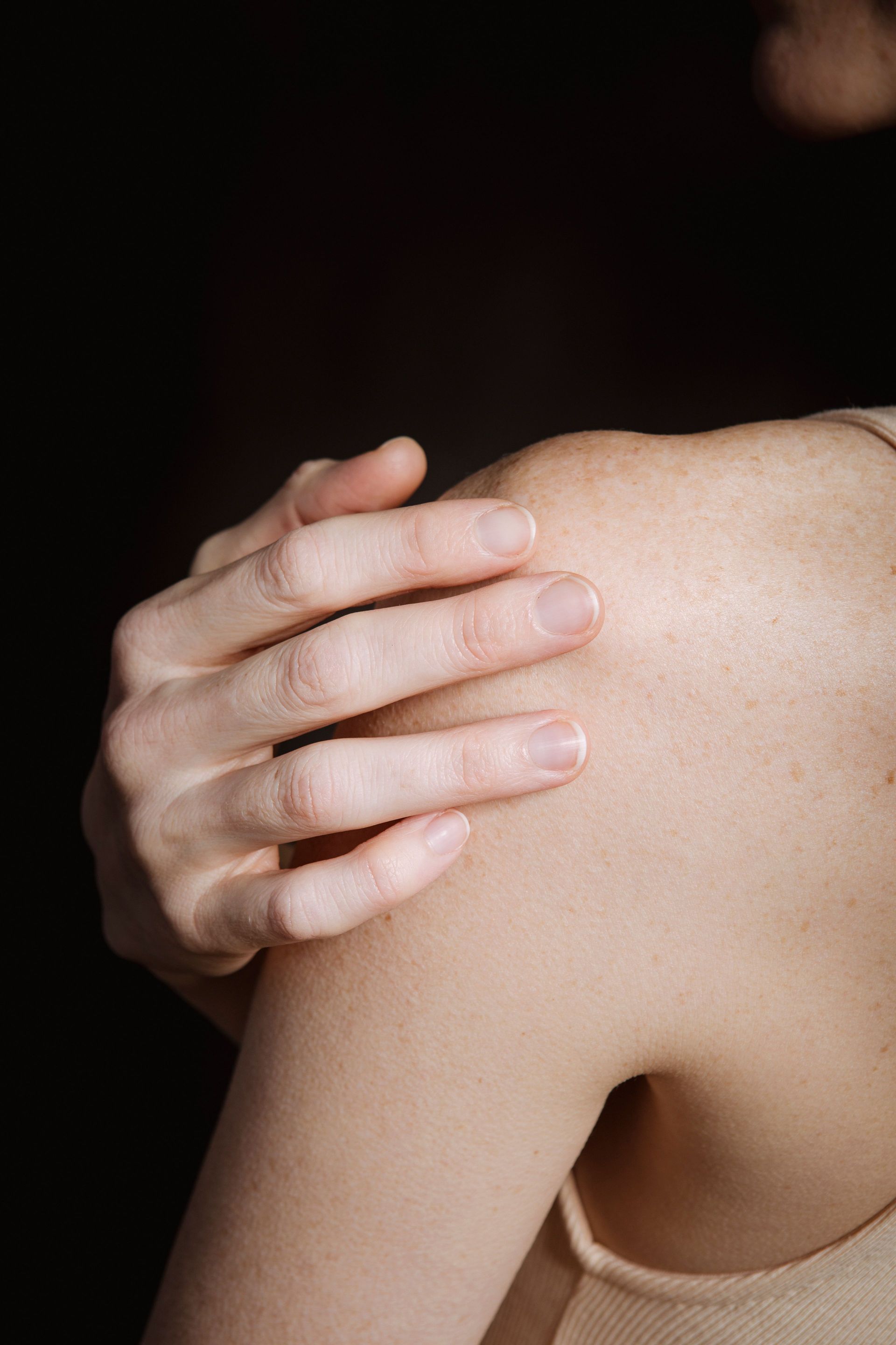 Hand touching a bare shoulder against a dark background