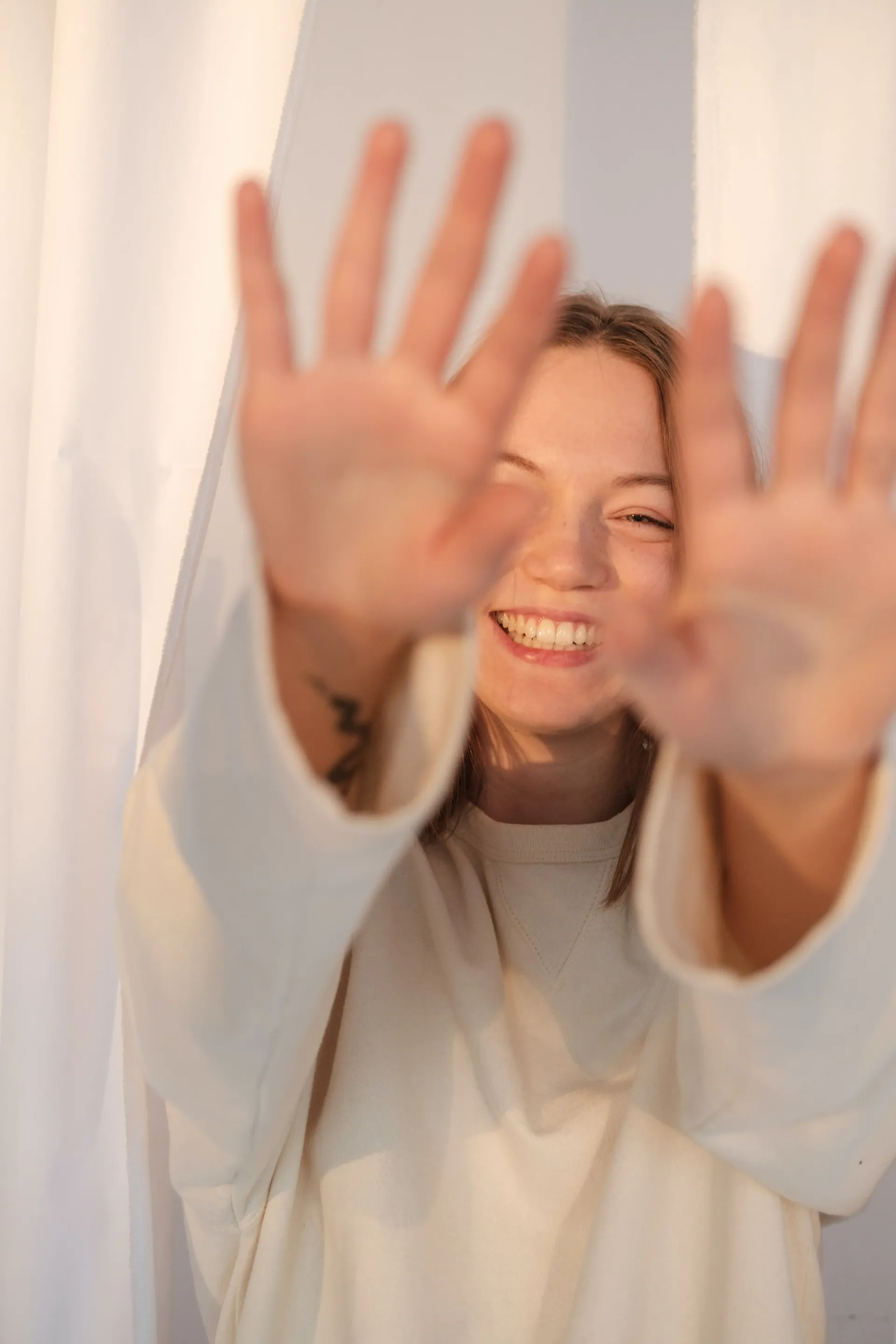 una donna in un maglione bianco sorride e tiene le mani in aria .