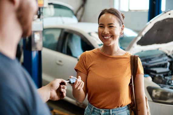 Smiling customer receiving car keys at an auto repair shop, with a car in the background