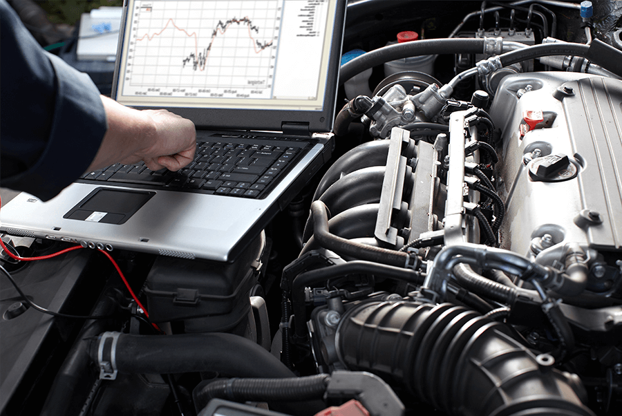 Mechanic using a laptop to diagnose a car engine in an open hood bay
