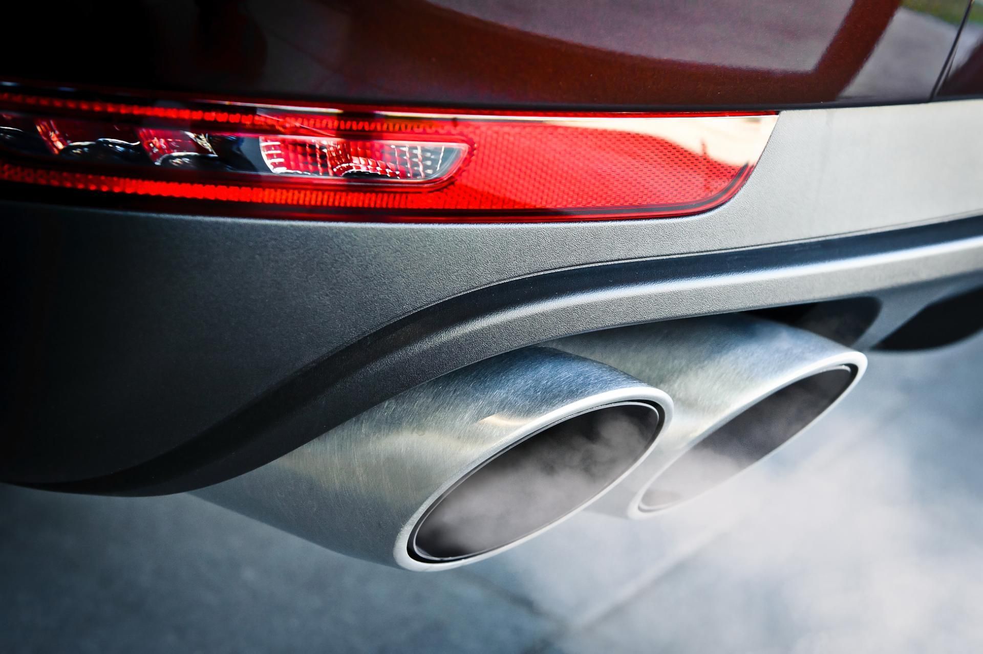 Close-up of a car’s rear with red taillight and twin chrome exhaust pipes emitting exhaust smoke