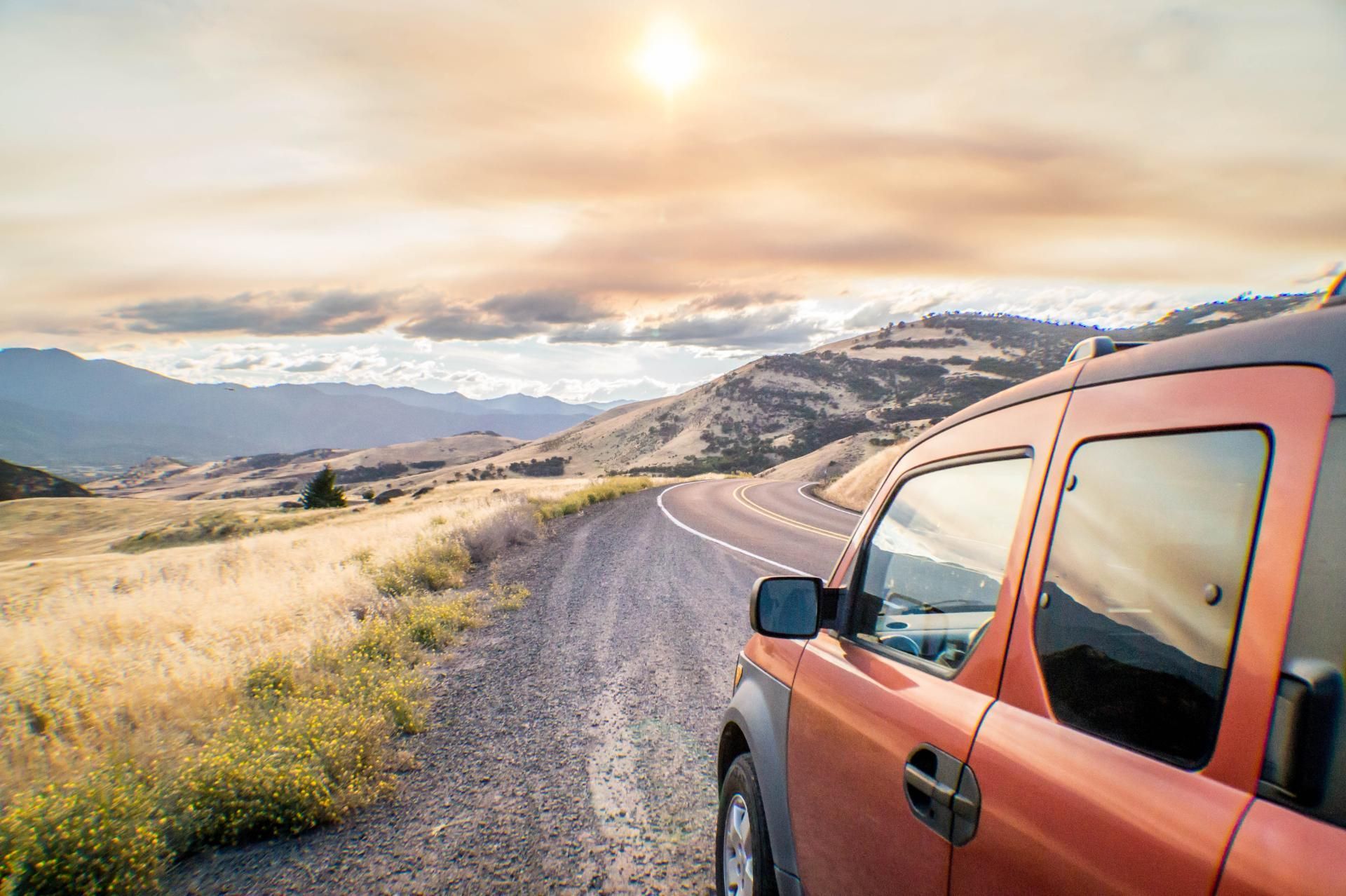 Red SUV on a gravel road in a sunlit mountain valley at sunset