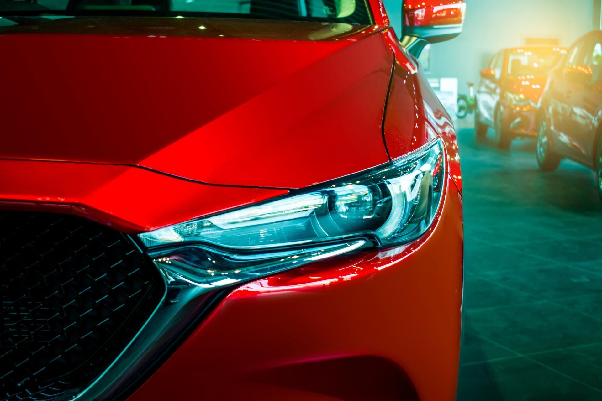 Red car front headlight in a parking garage, with a blurred car in the background.