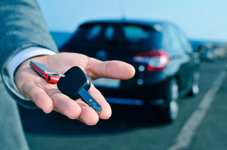 Mano che tiene le chiavi di un'auto davanti a un'auto nera, probabilmente durante un noleggio o un acquisto.
