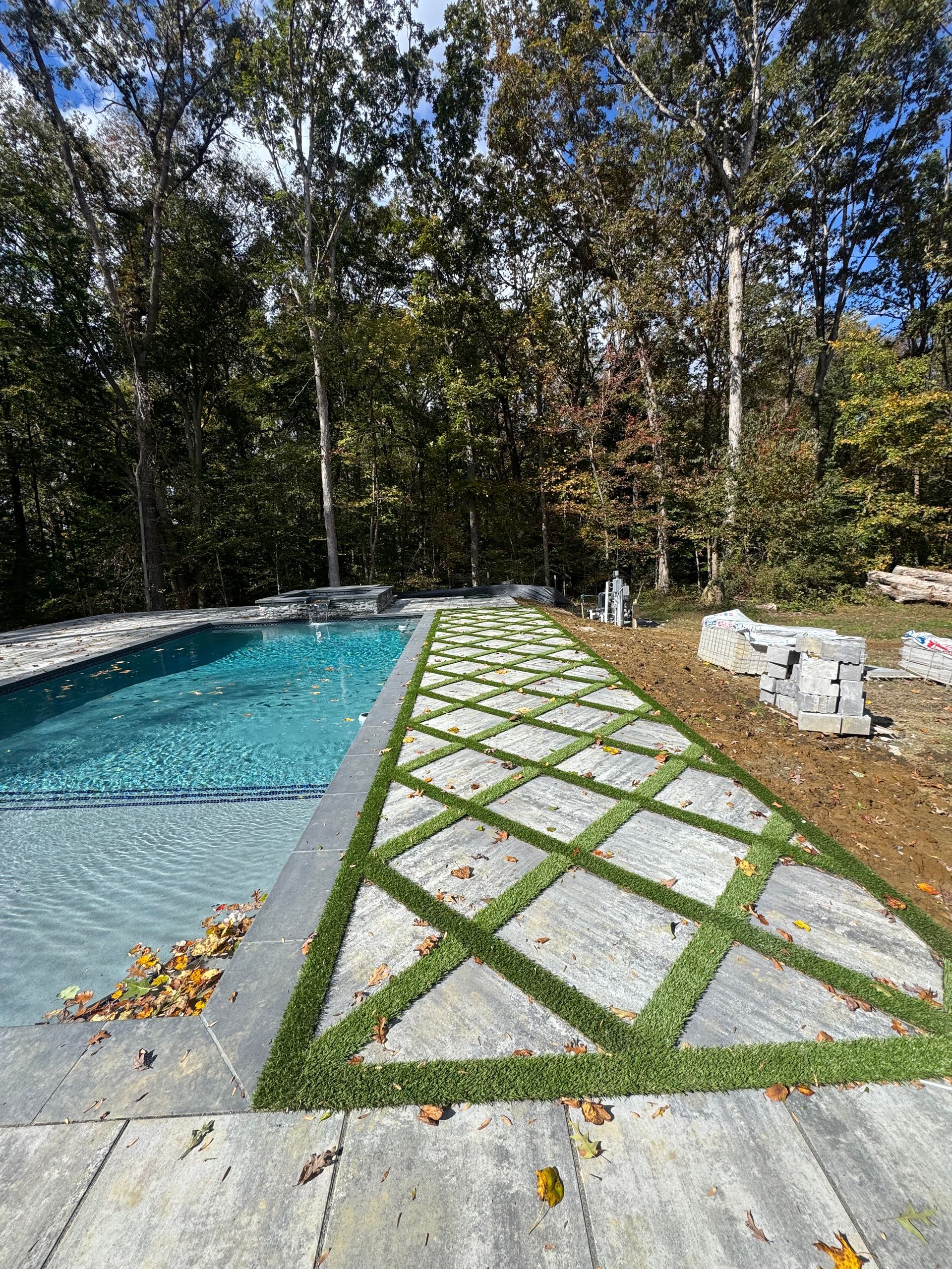 A swimming pool with a geometric patio featuring gray stone pavers set in a diamond pattern with grass inlays.