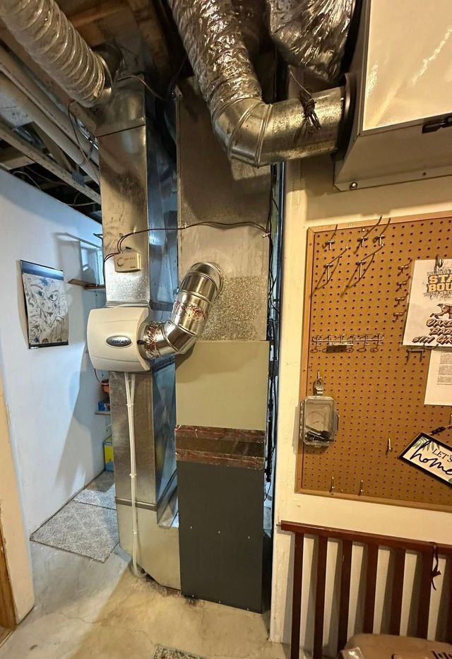 HVAC system in a basement featuring a metal furnace unit with a white humidifier attached and overhead ductwork.