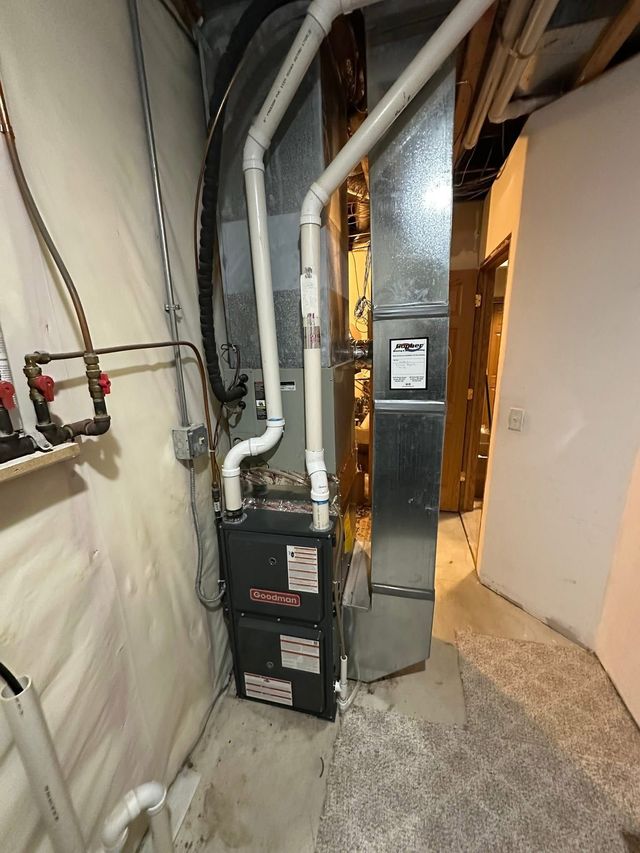 A vertical high-efficiency gas furnace and metallic ductwork in a residential basement.