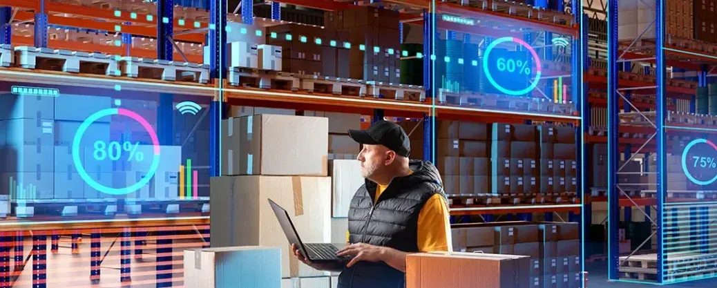 Warehouse worker using a laptop among shelves and holographic dashboard displays