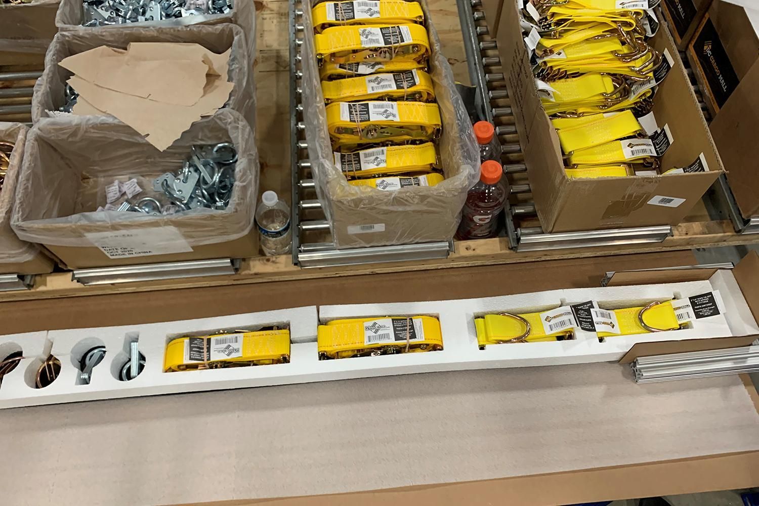 Tray of assorted packaged items and tools in bins on a worktable, with a long white strip below.