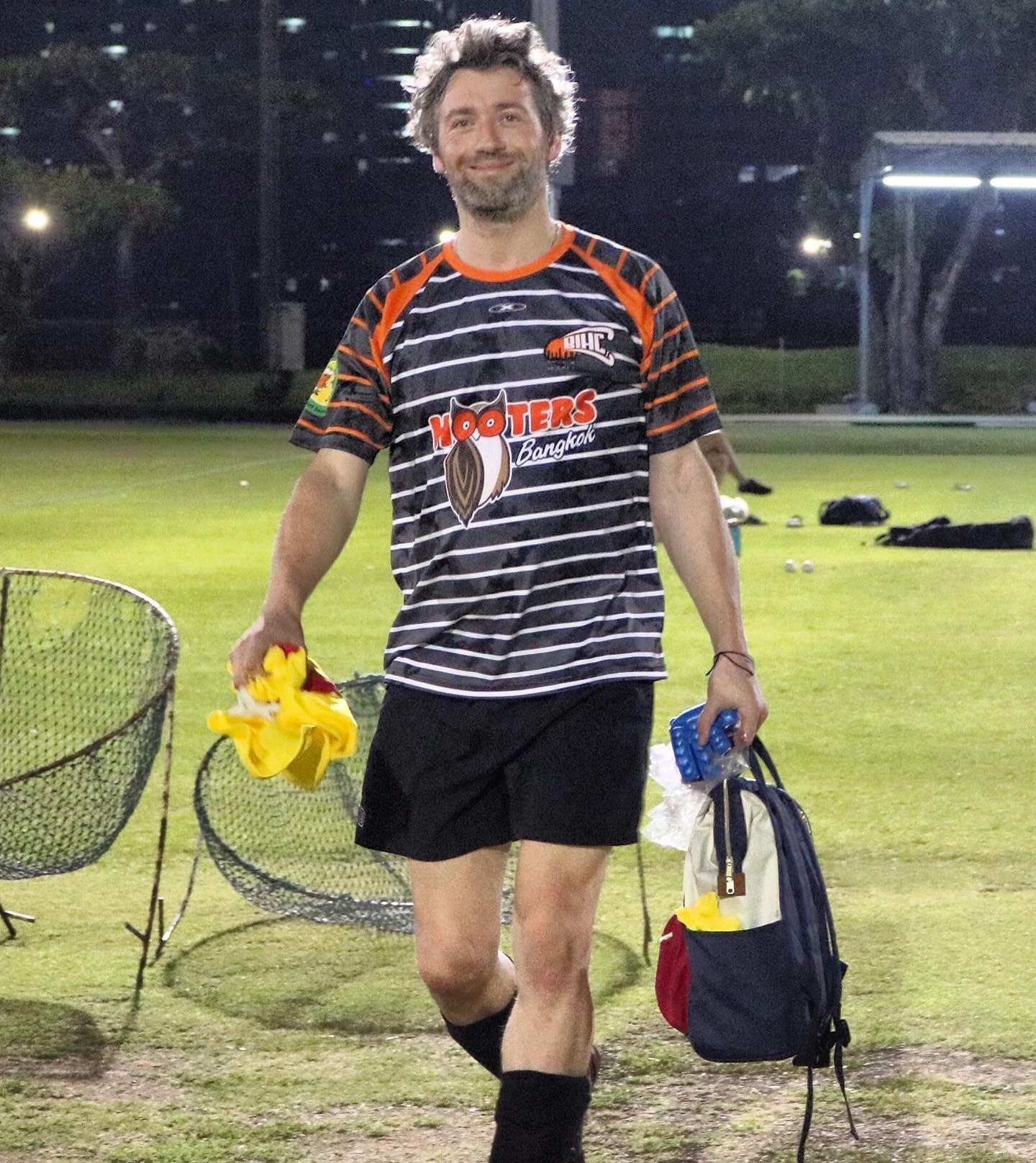 A man wearing a hooters shirt is walking on a field