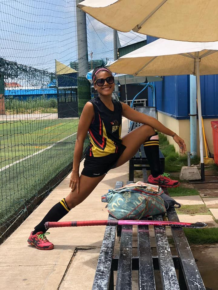 A woman is sitting on a bench stretching her legs.