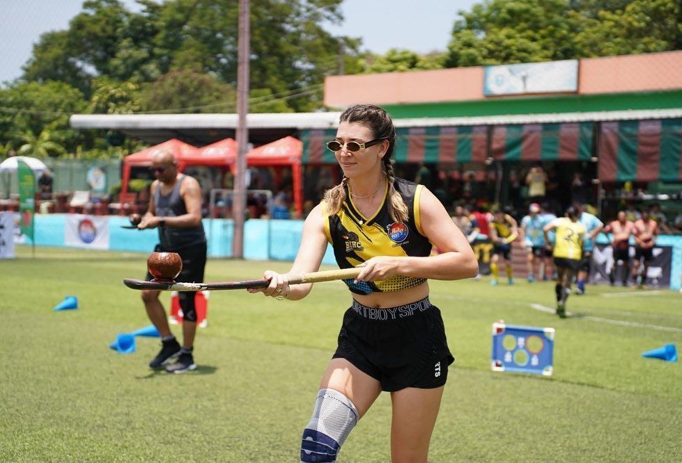 A woman is holding a wooden stick on a field.