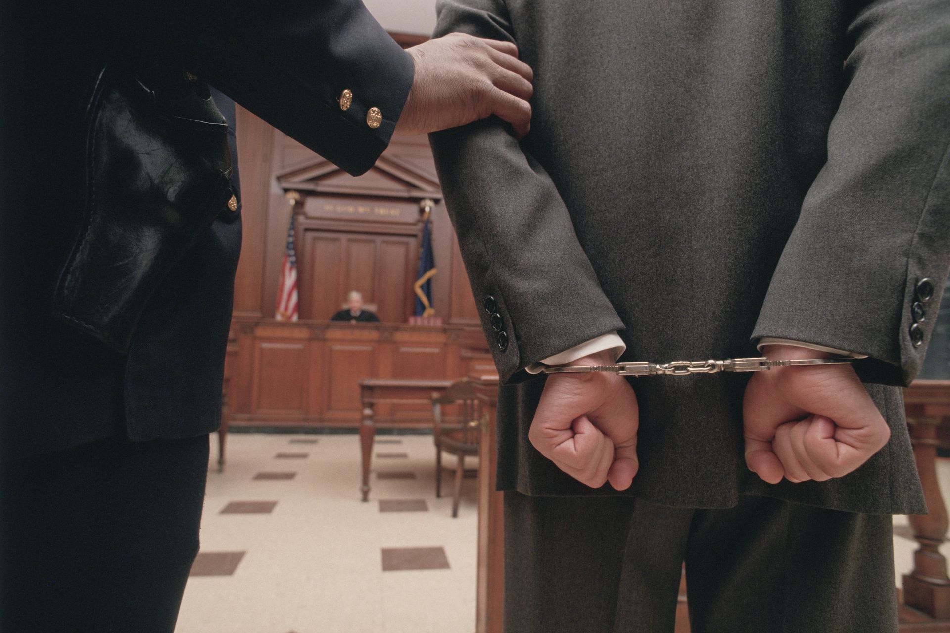 Man in handcuffs escorted by officer in courtroom.