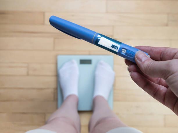 person standing on a scale holding semaglutide injection pen in their hand