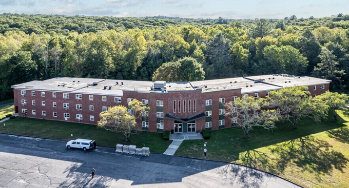 Aerial view of a red brick apartment building surrounded by trees and a parking lot.