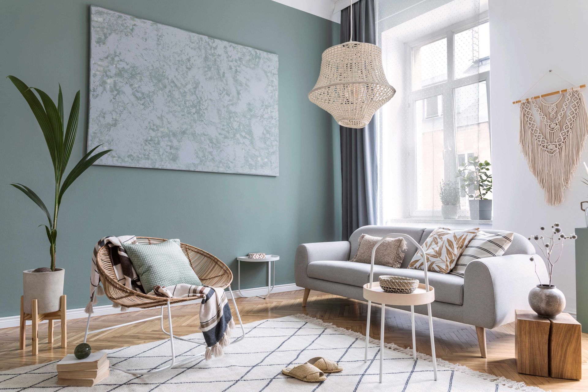 Bright airy living room with sage walls, white sofa, woven chair, rug, plants, and large abstract wall art