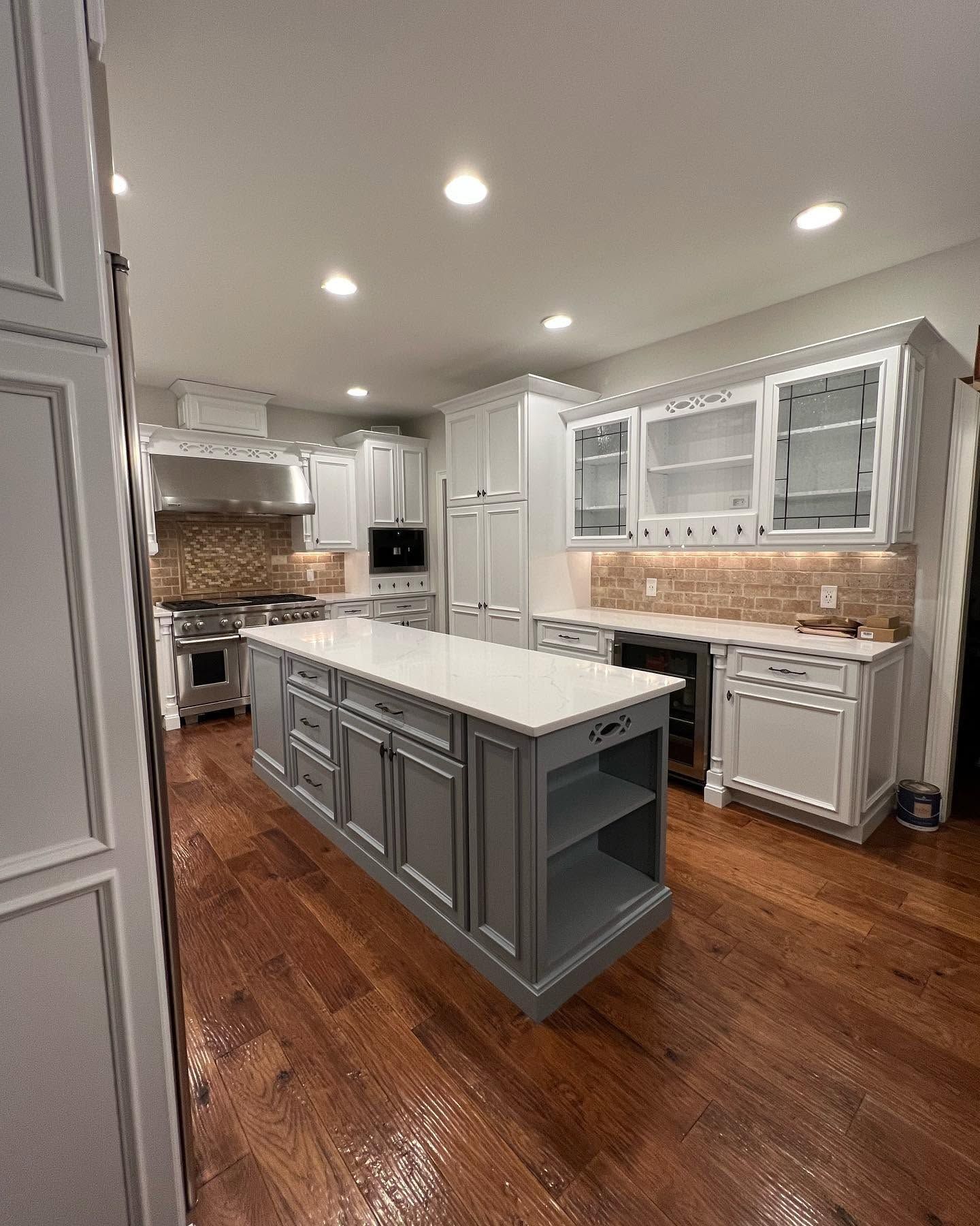 Modern kitchen with gray island, white cabinets, wood floors, and recessed ceiling lights