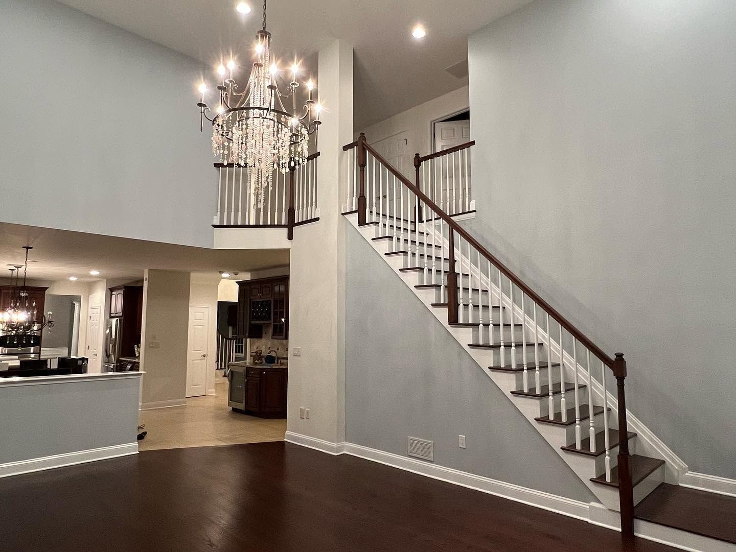Empty foyer with dark hardwood floors, chandelier, and staircase with white balusters