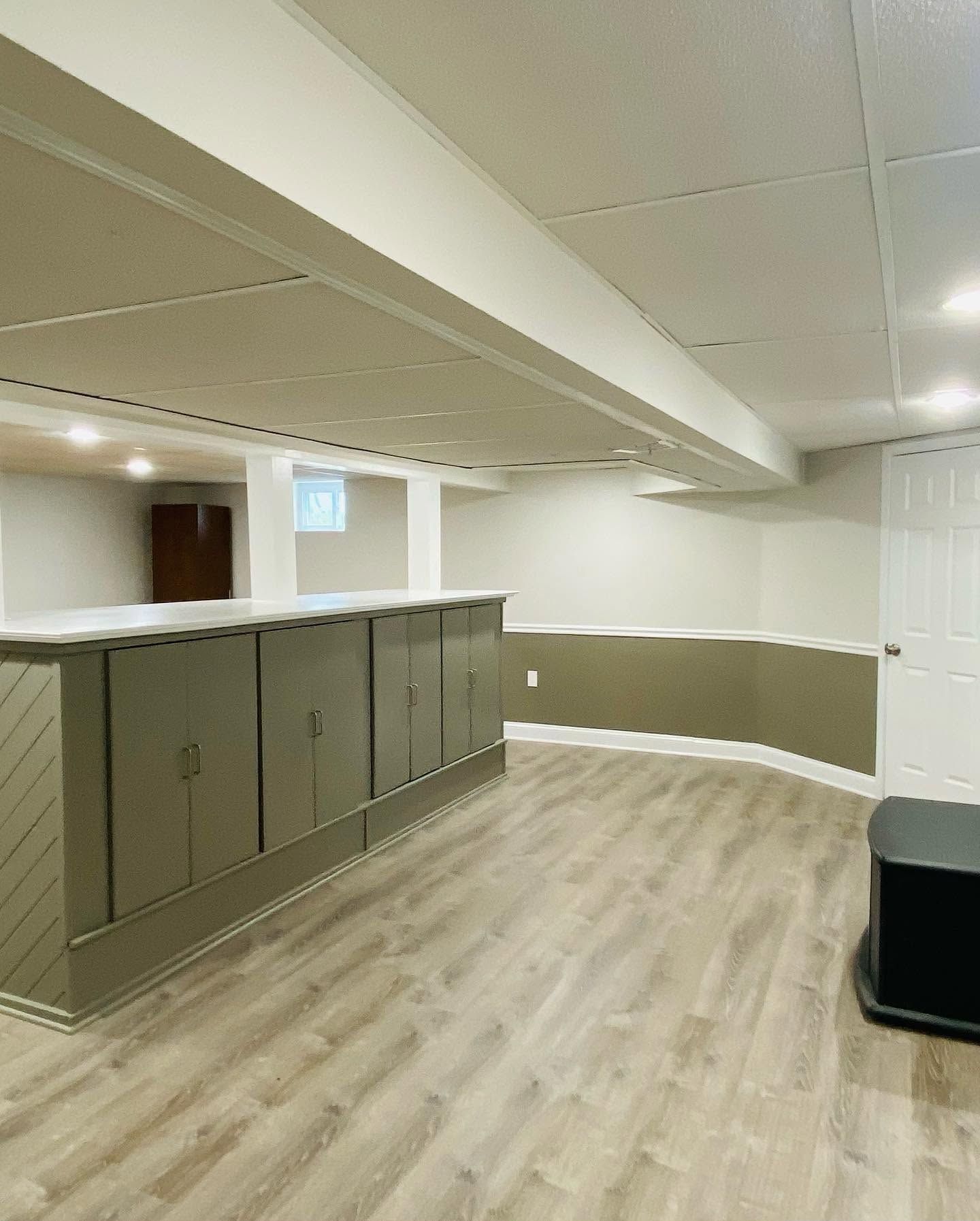 Empty basement room with gray cabinets, white ceiling, and light wood flooring