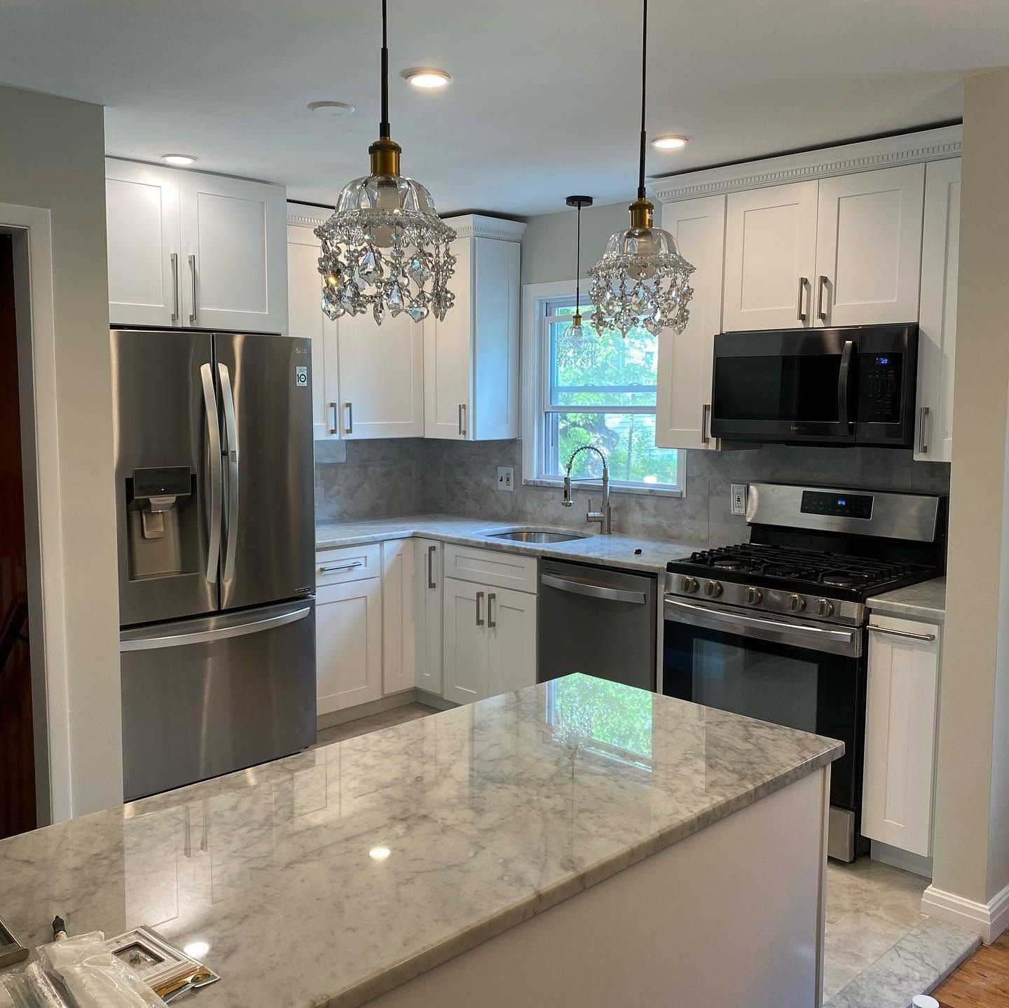 Modern white kitchen with marble island, stainless appliances, black stove, and pendant lights.