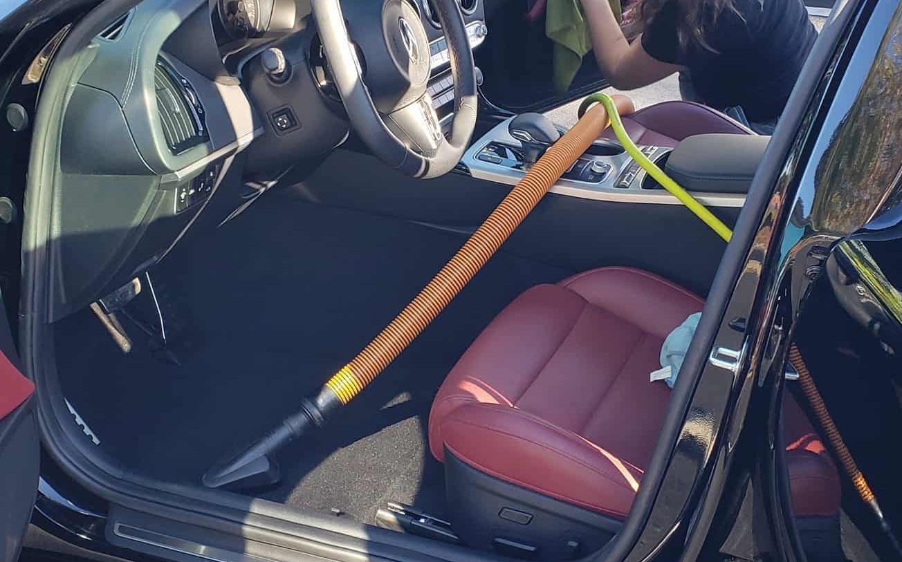 Interior car cleaning: vacuum in use. Red leather seat, black car.