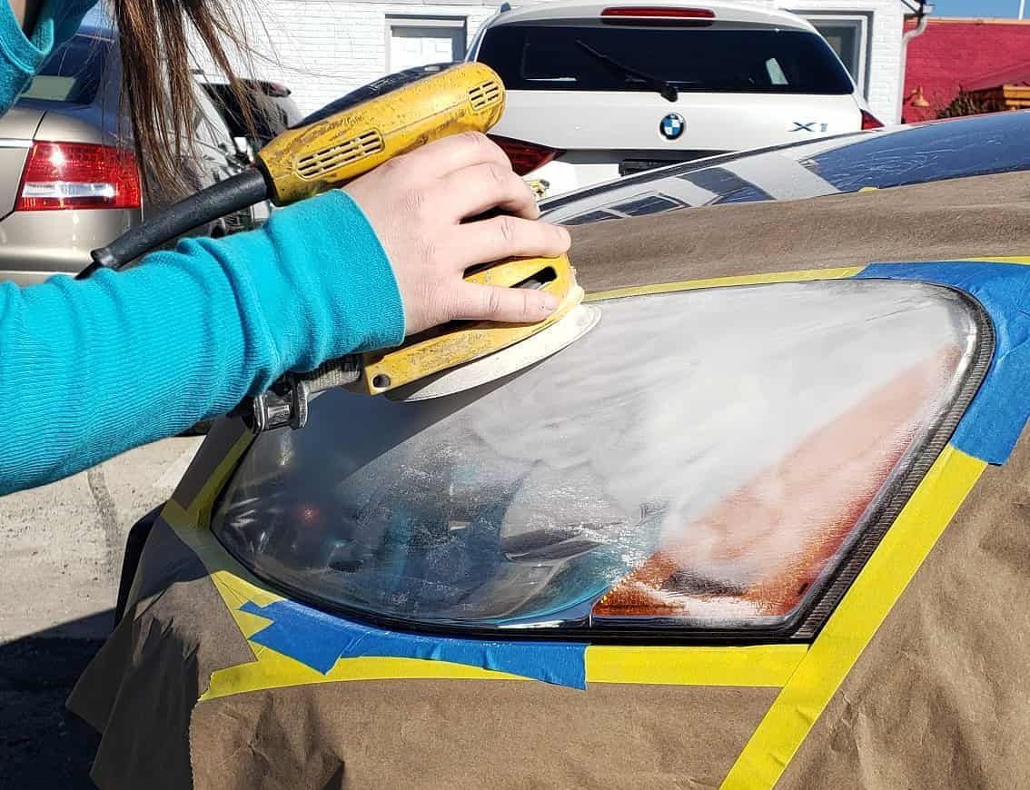 A person is sanding a car headlight with a sander.