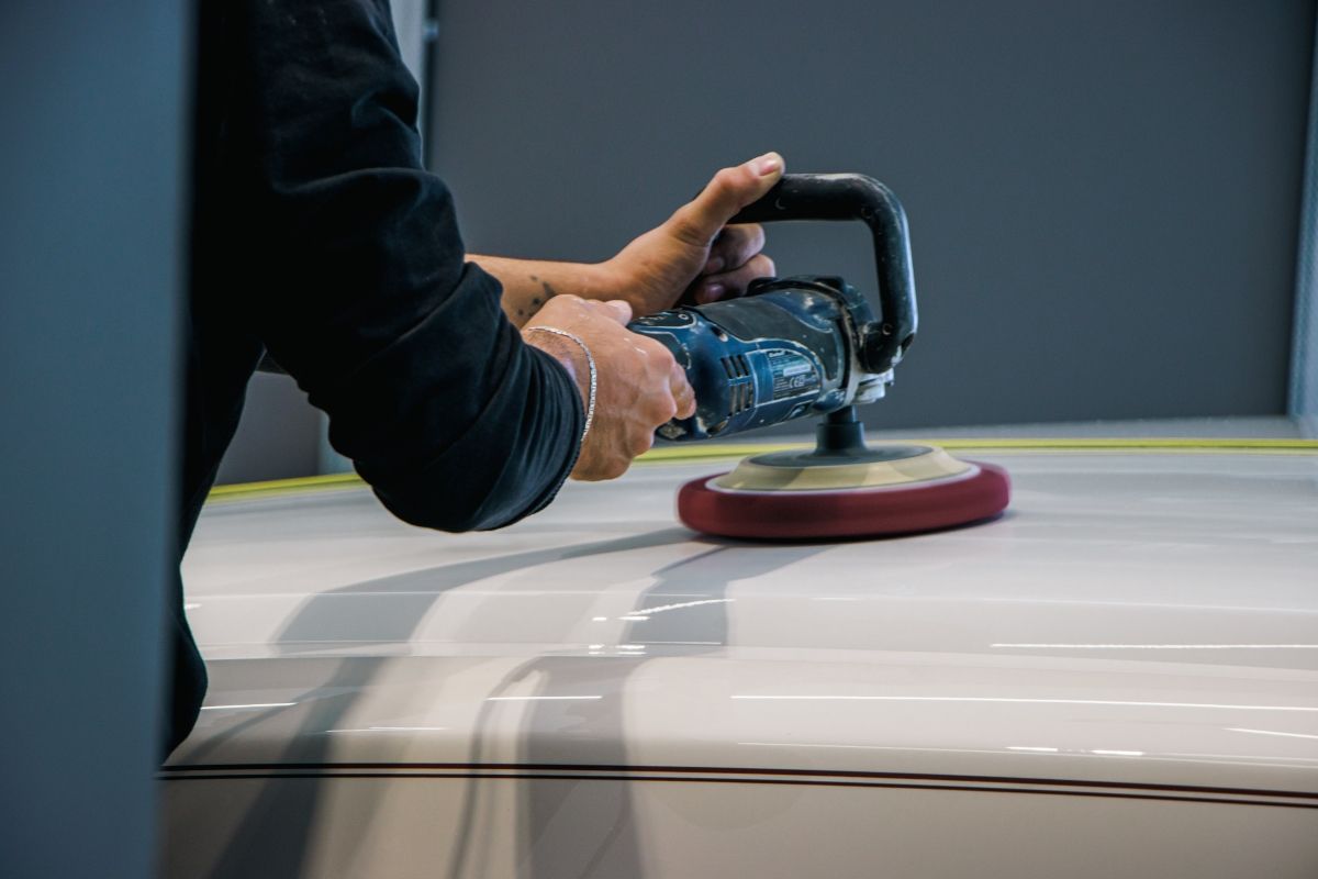 A person is polishing a white car with a machine.