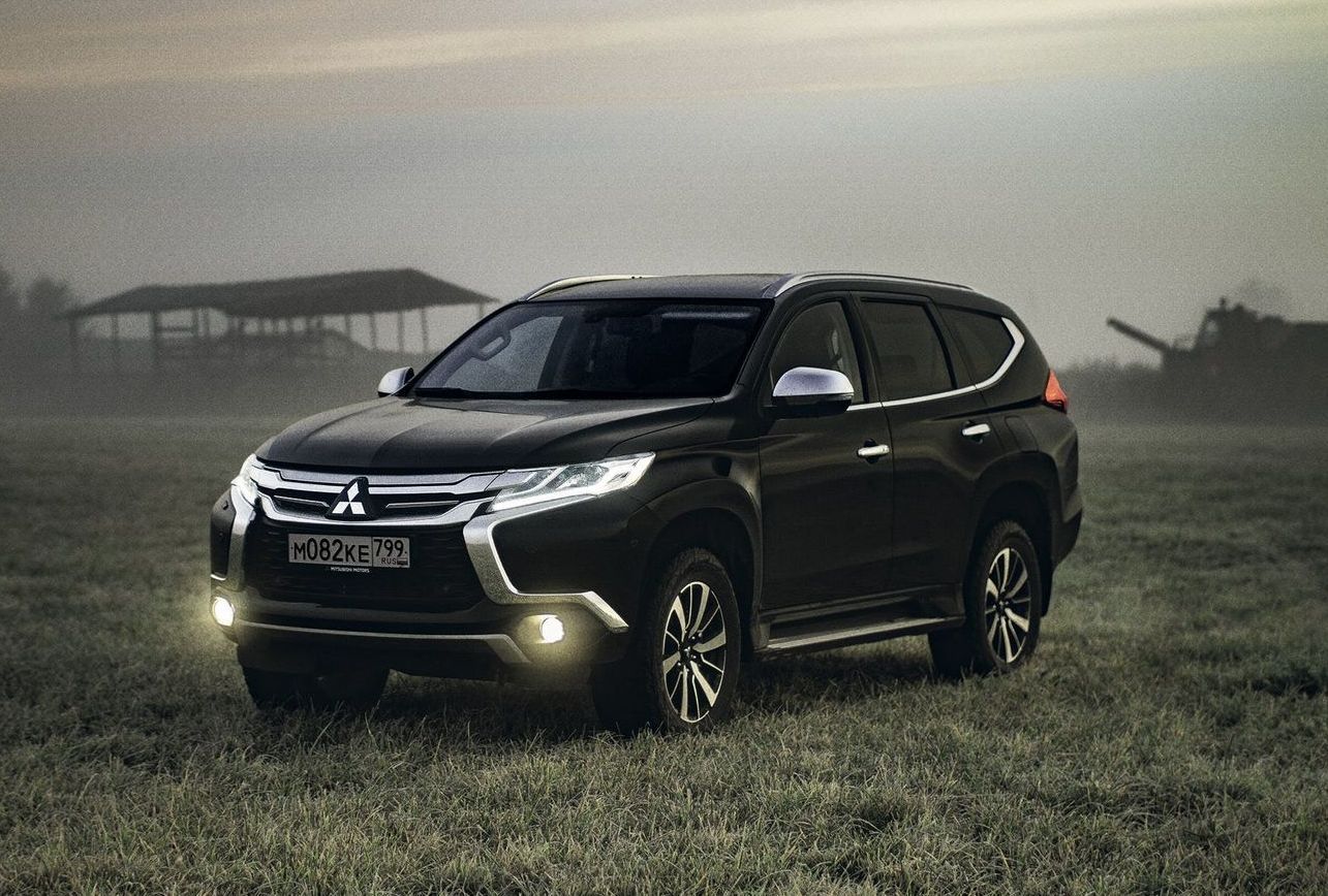 A black mitsubishi pajero sport is parked in a grassy field.