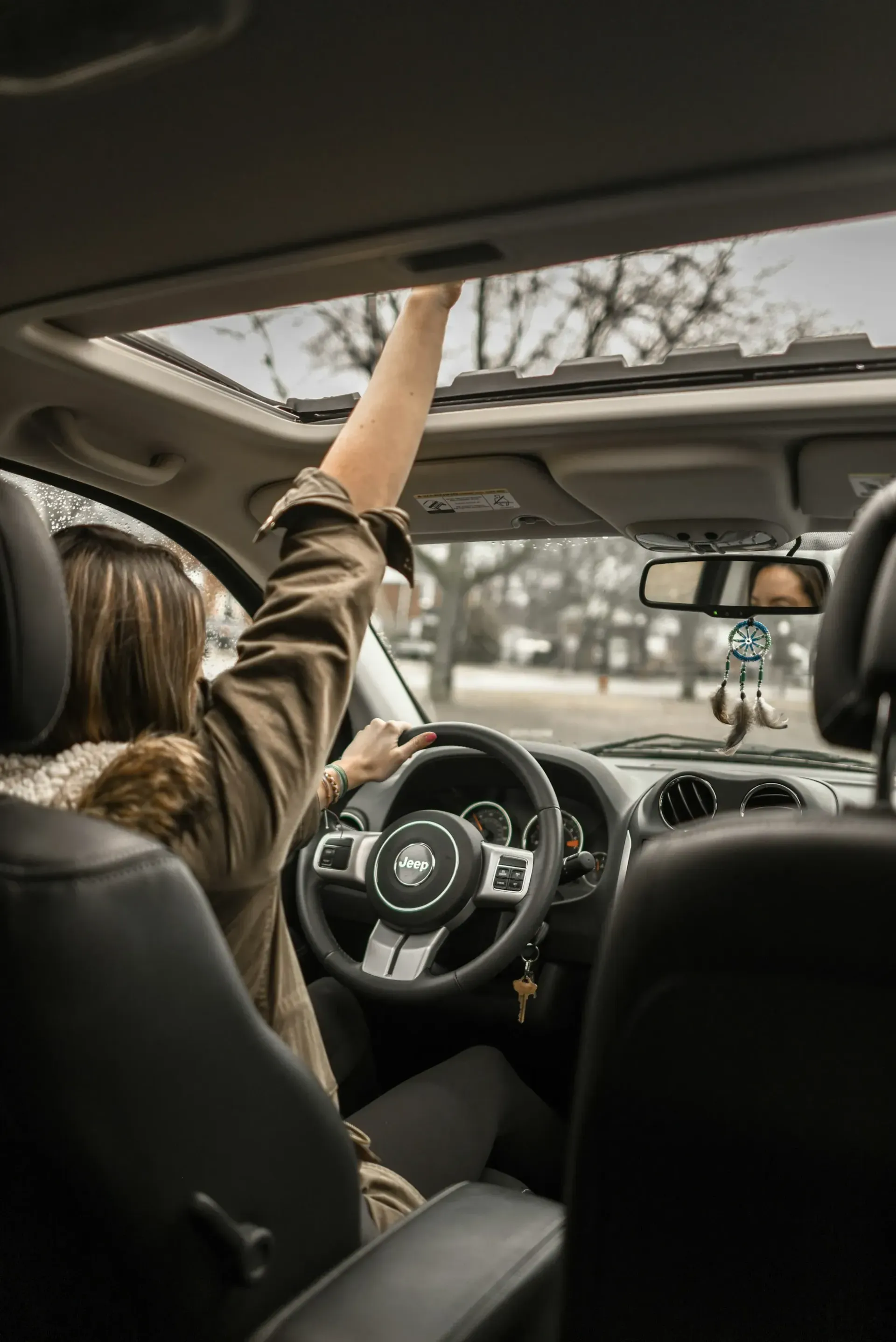 A woman is driving a car with her arms in the air.