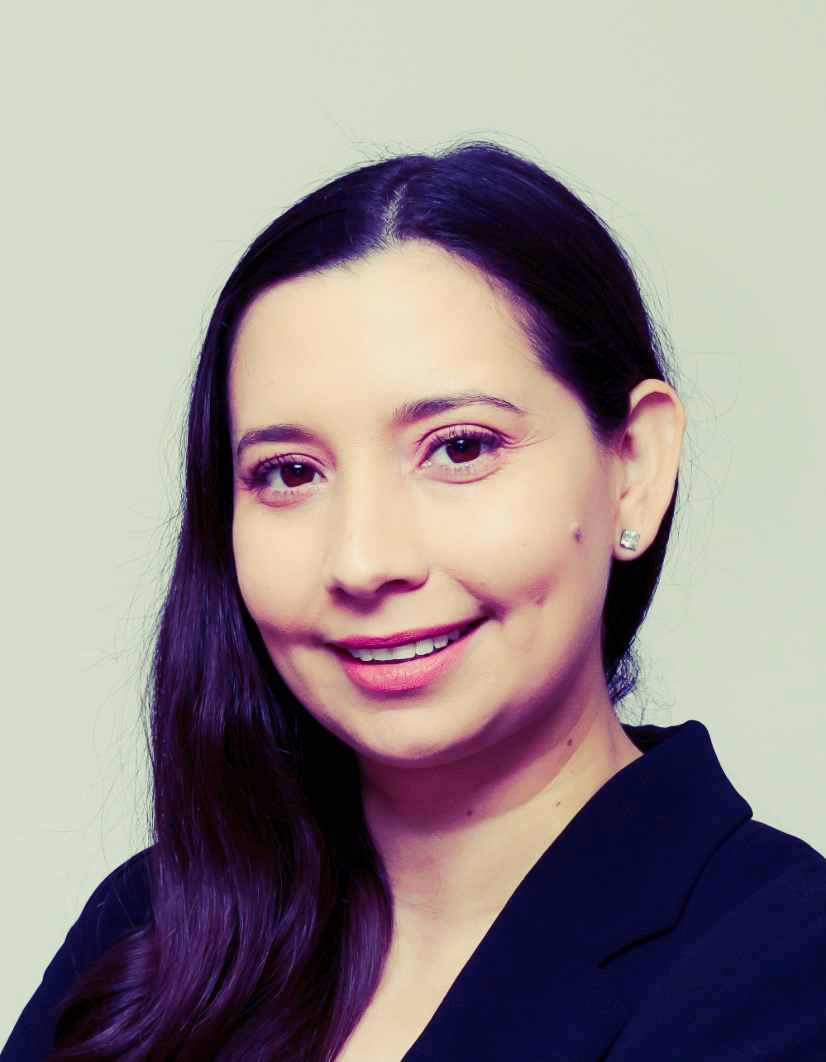 Woman with long dark hair smiles, wearing a dark blazer, against a light background.