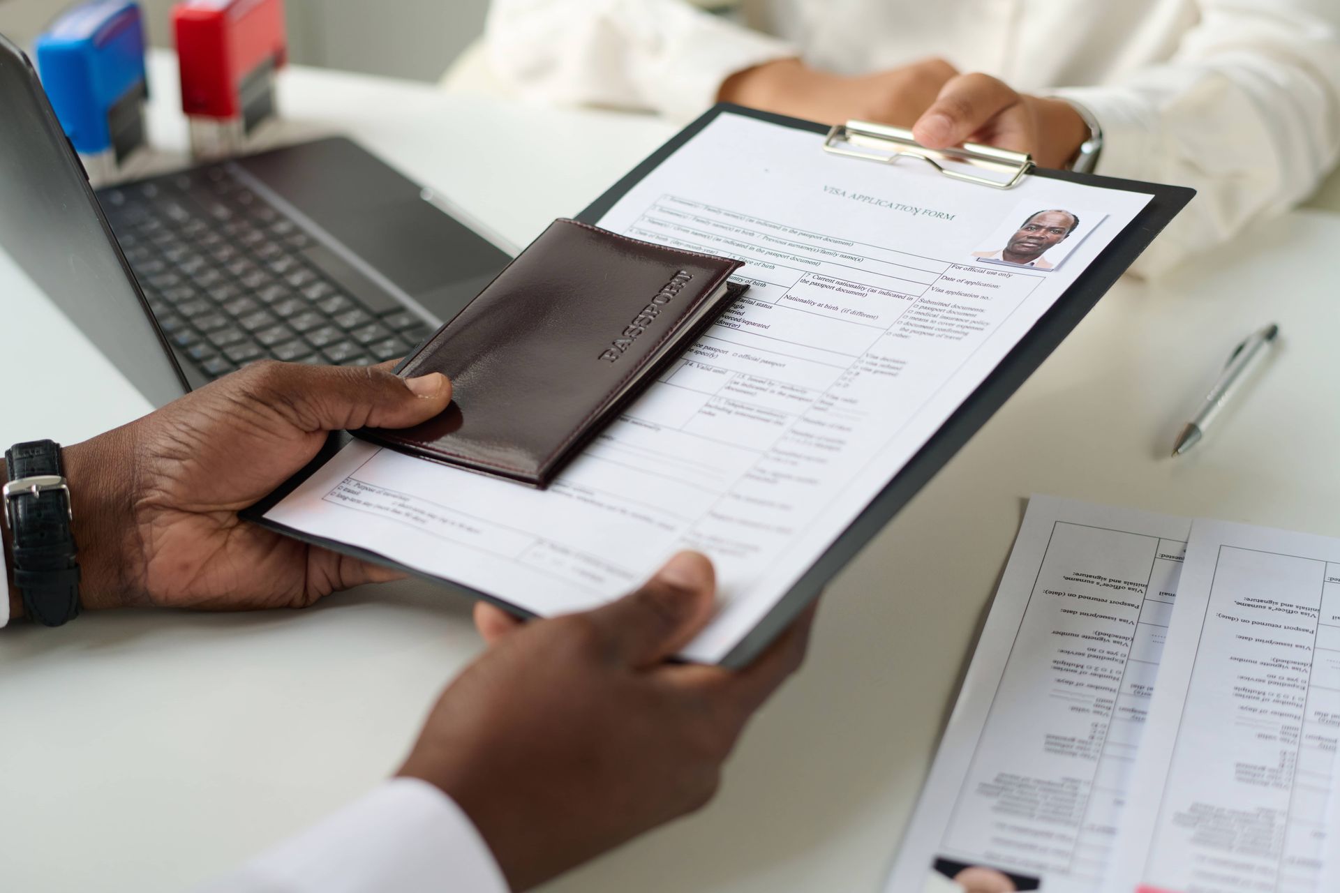 Hands exchanging a passport and clipboard during an ID check at a desk