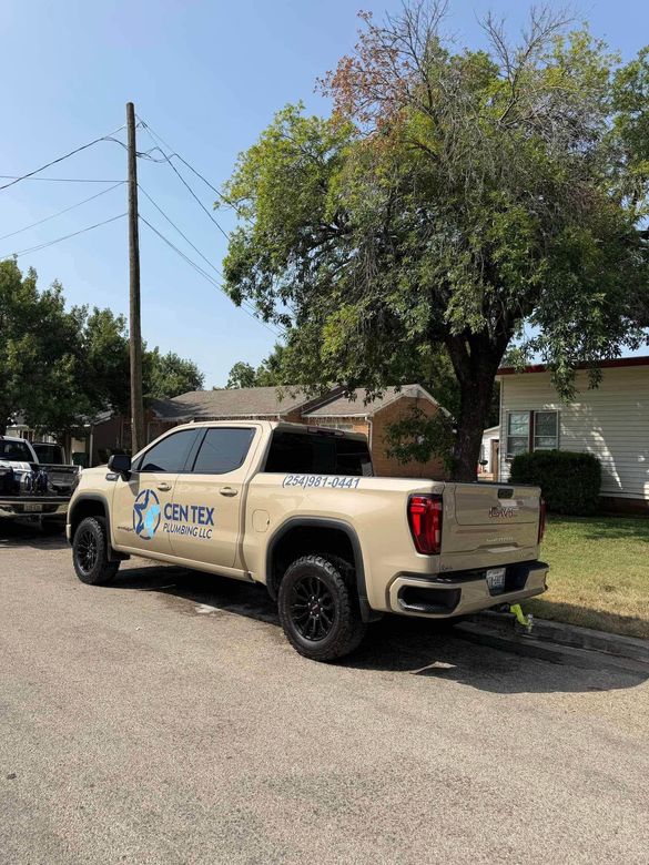 Beige utility pickup truck parked on a gravel lot beside a house and power lines.