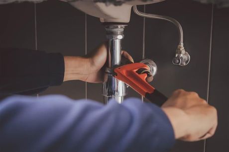 Hands using a red pipe wrench to tighten plumbing under a sink