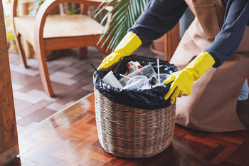 A person wearing yellow gloves is putting trash in a basket.