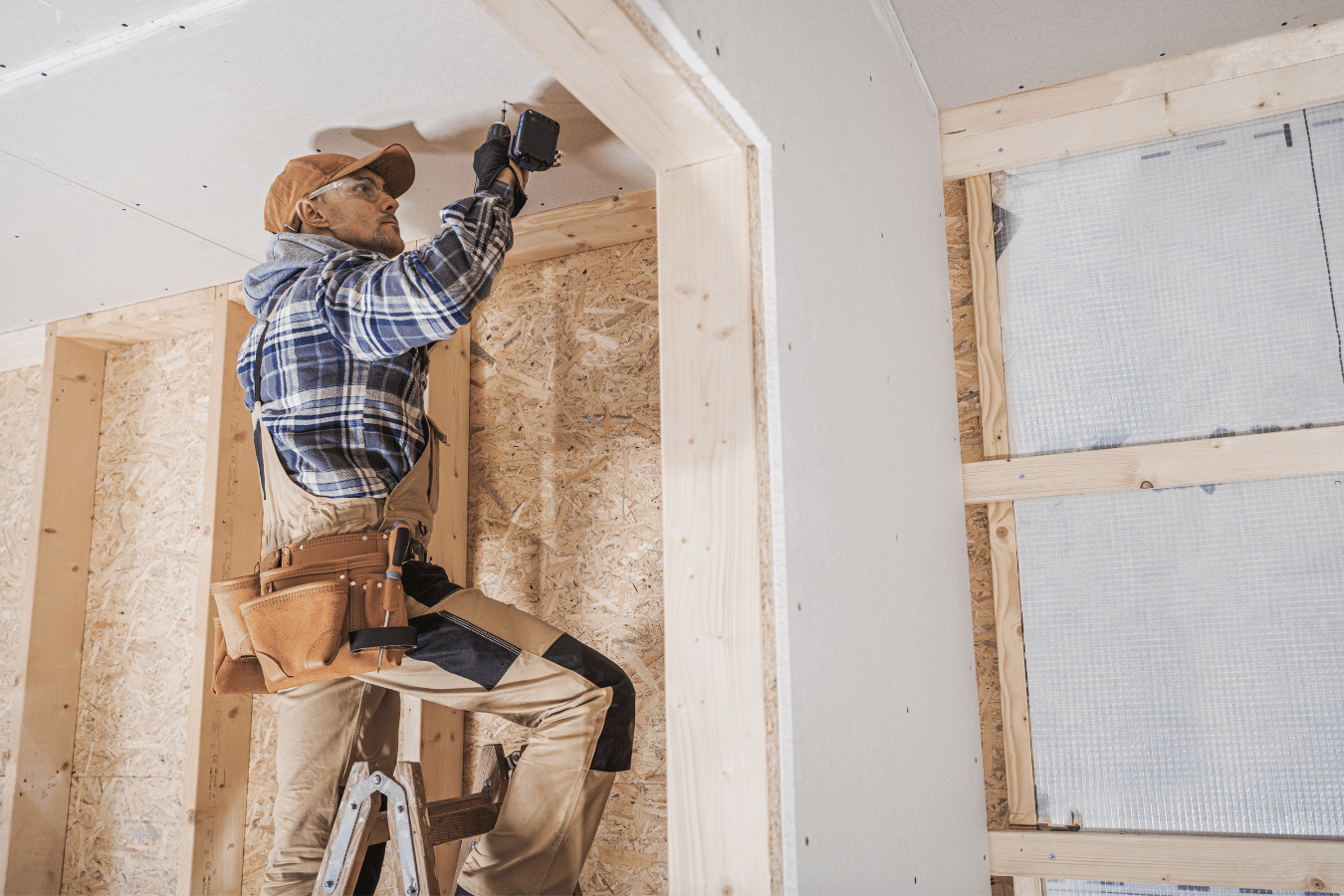 A man is standing on a ladder working on the ceiling of a house.