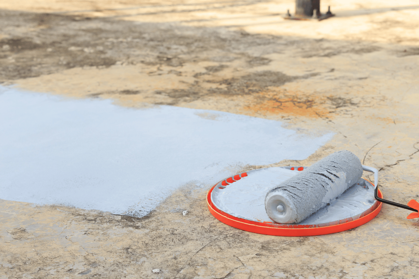 A paint roller is sitting on a tray on the ground.