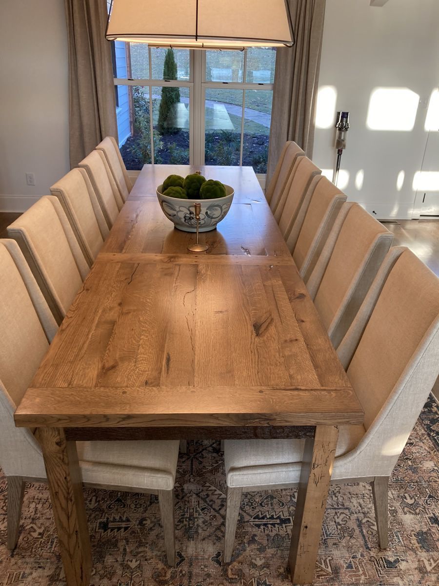 Wooden dining table with beige chairs in a bright room, centered by a bowl of greenery.