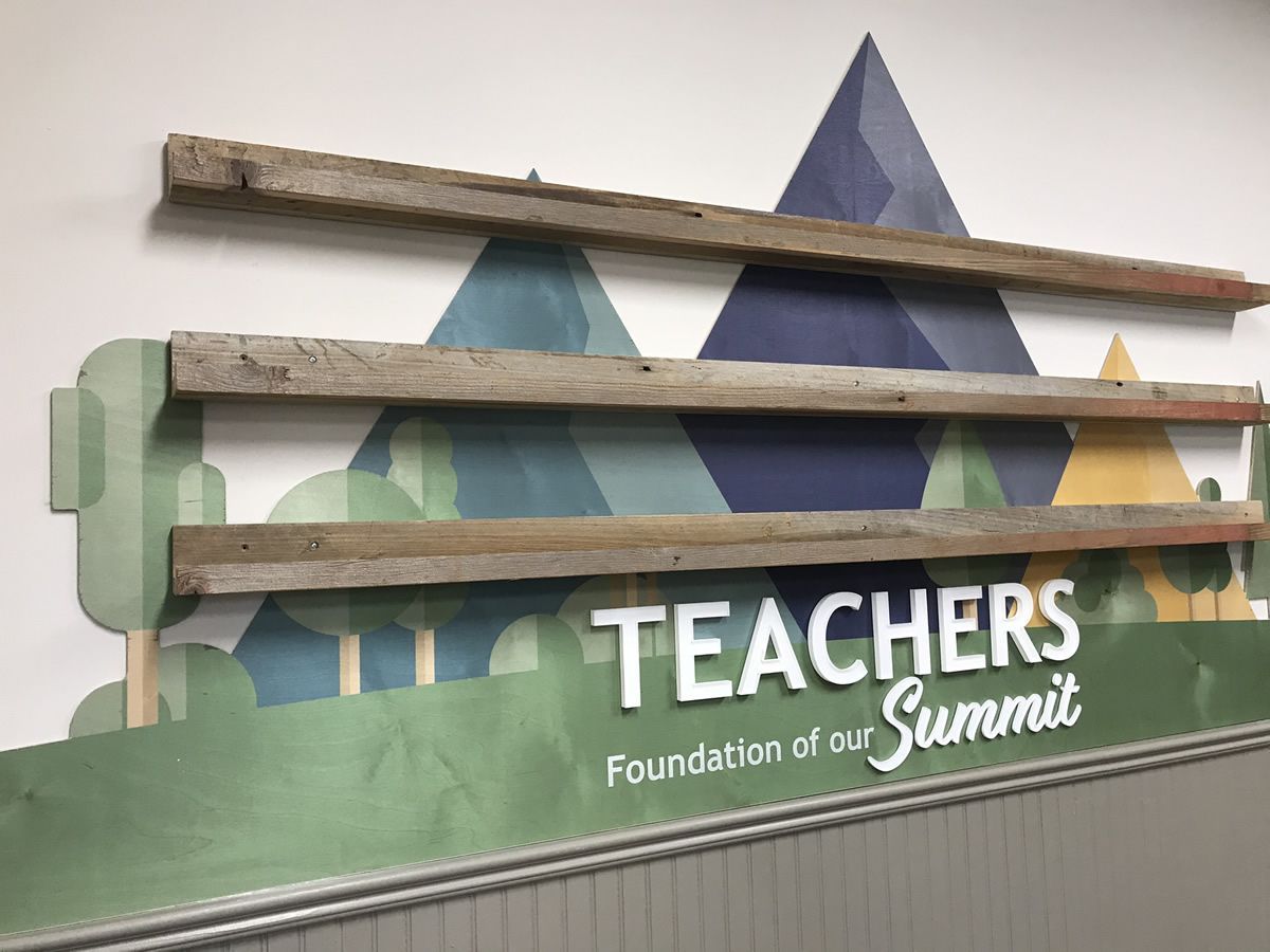 Wooden rack over a Teachers Foundation of our Summit sign with mountain graphic in green and blue