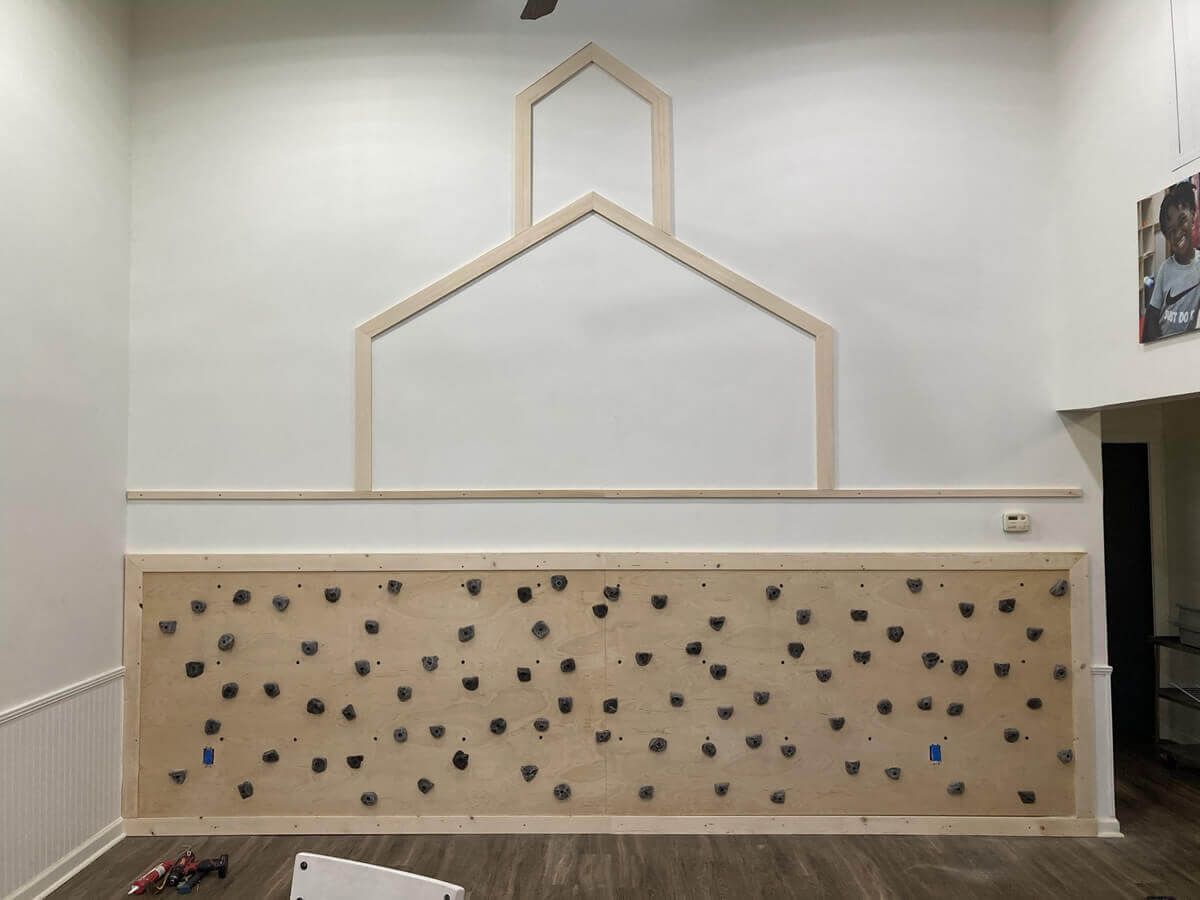 Indoor climbing wall with light wood frame and scattered black handholds on a beige panel