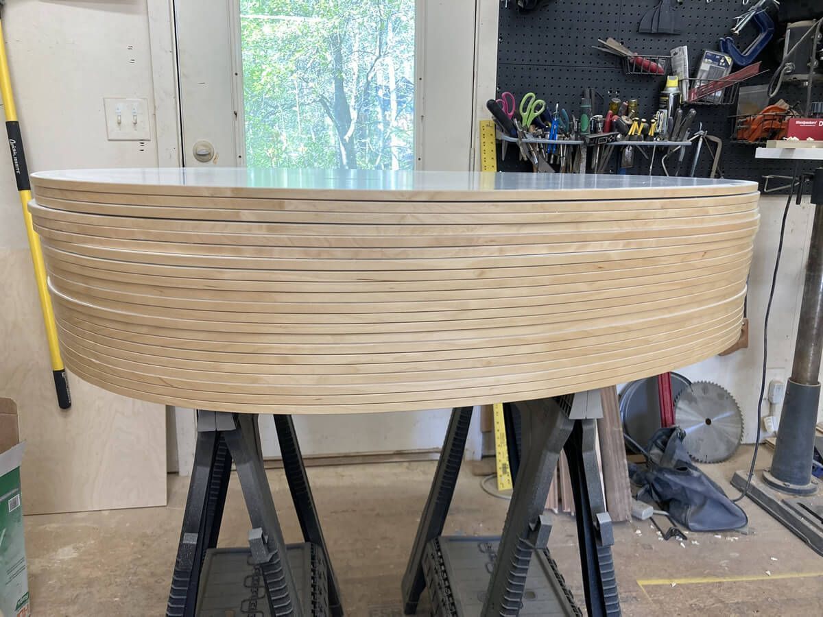 Curved woven wood panel on sawhorses in a workshop, with tools and a window in the background