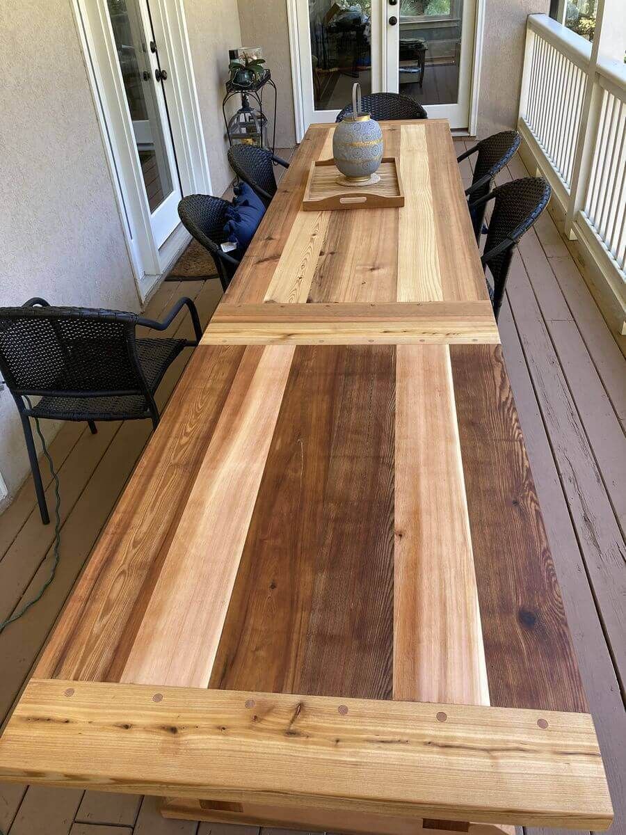 Long wooden dining table on a narrow covered porch with black chairs and a vase centerpiece